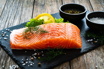 Fresh raw salmon steak with salt and fresh vegetables on wooden background
