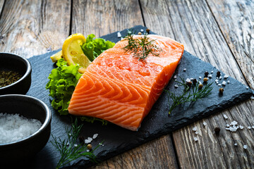 Fresh raw salmon steak with salt and fresh vegetables on wooden background
