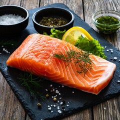 Fresh raw salmon steak with salt and fresh vegetables on wooden background
