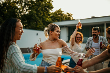 Group of friends having a blast in a sunny backyard. They're dancing and chilling with drinks by the pool.