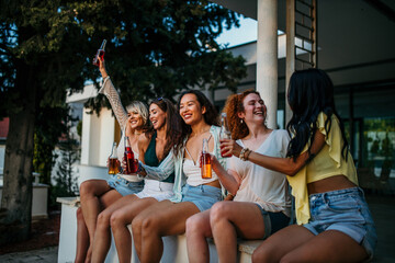 A group of girlfriends cherishing the moment with drinks in hand, enveloped by the beauty of a...