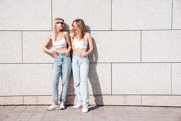 Two young beautiful smiling hipster female in trendy summer white top and jeans clothes. Carefree women posing in the street. Positive models having fun outdoors. Cheerful and happy. In sunglasses