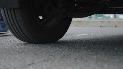Driver takes diamond-shaped jack from under car after replacing flat tire on road. Amateur maintenance of personal car due to an unexpected breakdown on road trip.