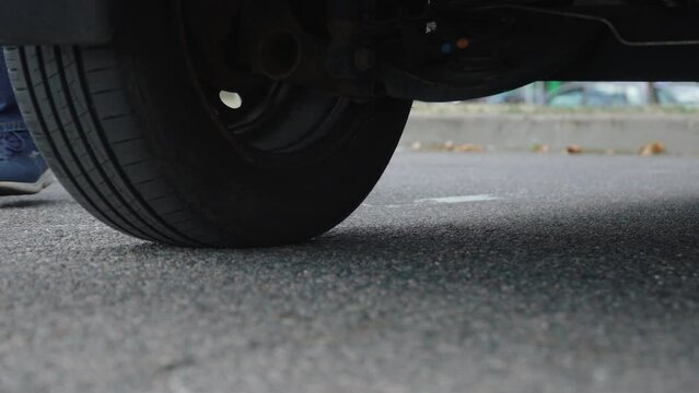Driver takes diamond-shaped jack from under car after replacing flat tire on road. Amateur maintenance of personal car due to an unexpected breakdown on road trip.