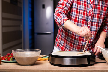 Woman cooking delicious crepe on electric pancake maker in kitchen, closeup