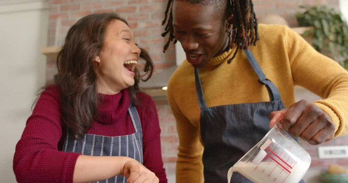 Happy diverse couple in aprons having fun baking in kitchen, slow motion