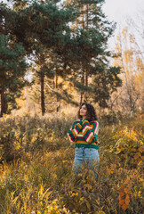 Lady in a striped knitted sweater stands near a tree in the forest.