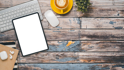 Wooden desk with blank screen tablet, keyboard, mouse, earphone, notebook and cup of coffee, Top view flat lay with copy space.