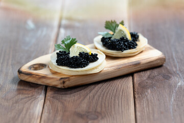 Black sturgeon caviar on pancakes on a wooden plate close-up