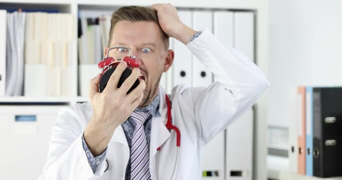 Young male doctor looks at alarm clock and shouts. Overtime and deadline in medicine concept