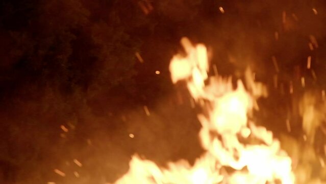 Intentional light blur: within the serene night, blazing, fervent flames burst forth from a crackling bonfire, with fascinating sparks fiying away. Captured in slow-motion.