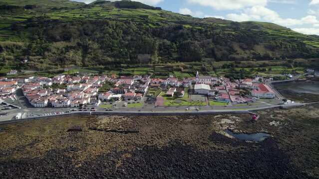 Drone pullback view of Lajes do Pico coastal village on rugged shoreline, Azores