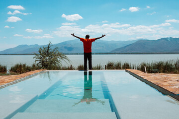 A man on an infinity swimming pool against Lake Jipe at border of Kenya Tanzania seen from Tsavo...