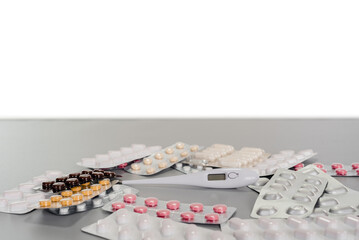 white digital thermometer surrounded by blisters of pills on a gray table with copy space background
