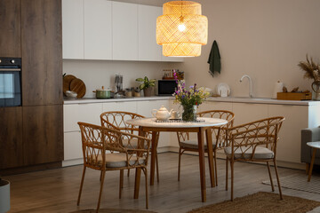 Interior of modern kitchen with glowing lamp and flower vase on dining table