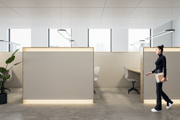 Happy young businesswoman walking in modern coworking office interior with empty mock up place, partitions and workplaces, window with city view and daylight.