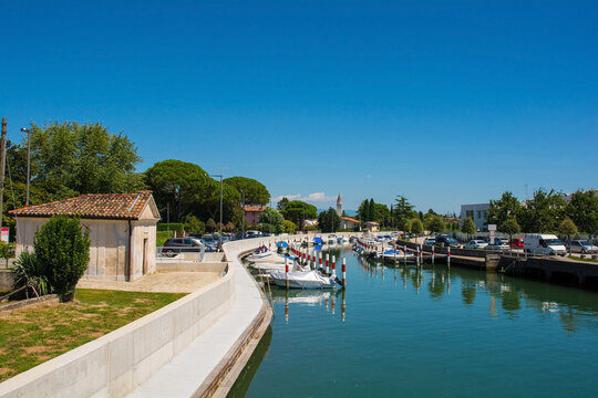 The marina in Aquileia in Friuli-Venezia Giulia, north east Italy. August. The Cappelle delle Vergini Aquileiesi chapel is foreground left