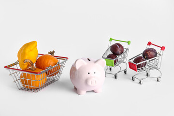 Piggy bank and shopping carts with healthy food on white background