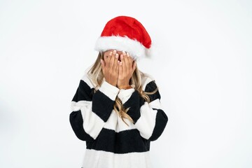Beautiful hispanic woman wearing christmas hat and striped knitted sweater covering her face with her hands, being devastated and crying. Sad concept