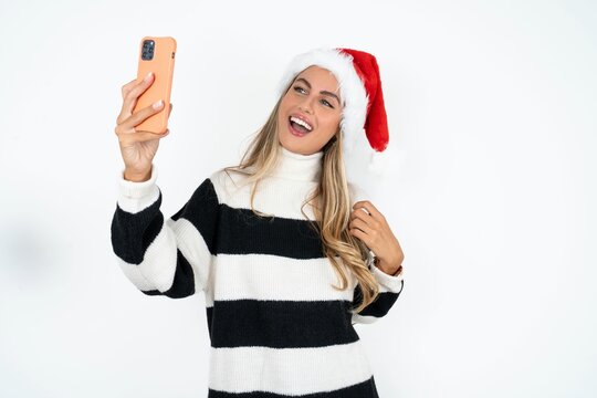 Beautiful hispanic woman wearing christmas hat and striped knitted sweater smiling and taking a selfie ready to post it on her social media.
