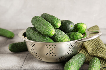 Colander with fresh cucumbers on table