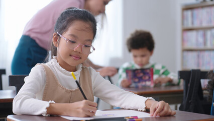 Asian school girl in glasses studying, writing notes in notebook at classroom. Schoolgirl studying and preparing for exams. little pupil writing at desk in classroom. Education knowledge concept