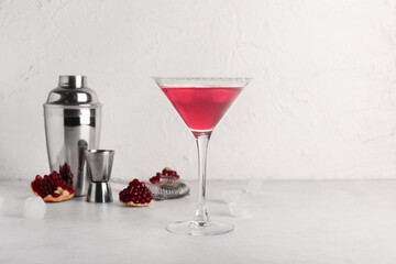 Glass of Cosmopolitan cocktail with pomegranate and shaker on white background