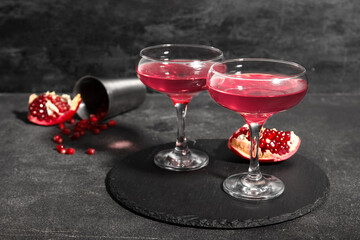 Board with glasses of Cosmopolitan cocktail and pomegranate on black background