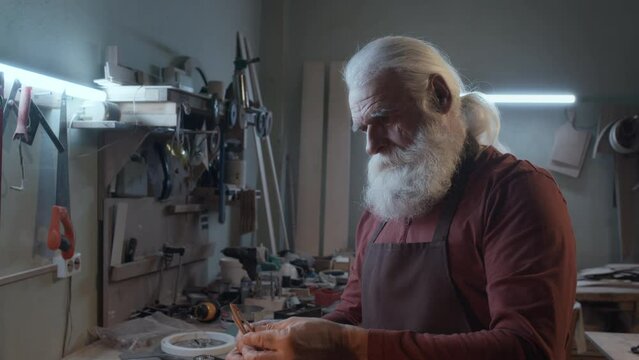 Medium close-up shot of elderly Caucasian woodworker searching for different sizes of brushes in his toolbox