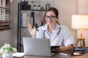 Young lady doctor in white medical uniform using laptop talking video conference call with senior...