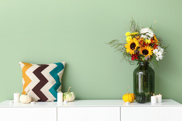 White sideboard with bouquet of autumn flowers near green wall