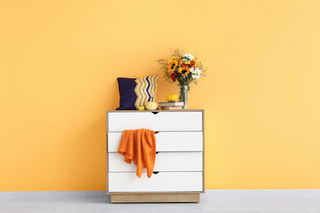 White chest of drawers with bouquet of autumn flowers and pumpkins near orange wall