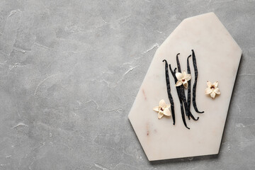 Board with aromatic vanilla sticks and flowers on grey background