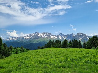 Fototapeta premium Snow-Capped Mountains with Green and Dry Grass, Clouds, and a Stunning Sky