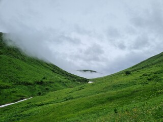 Snow-Capped Mountains with Green and Dry Grass, Clouds, and a Stunning Sky