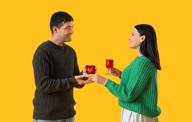 Young couple with glasses of mulled wine on yellow background