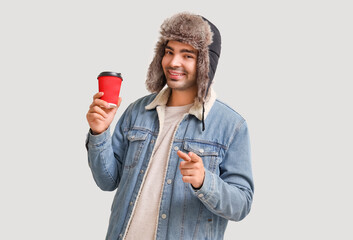 Young man with cup of mulled wine pointing at viewer on light background