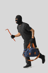 Male thief with crowbar and bag on grey background