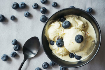 Ice cream with fresh blueberries in a dark plate next to a spoon