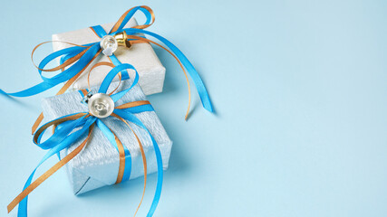 Two gift boxes wrapped in white and blue silver paper with blue and gold ribbon bows and bells. Blue background, top view. Christmas and New Year gifts, Boxing Day.