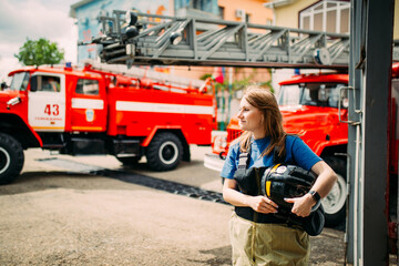 Female firefighter in protective uniform standing near red fire truck