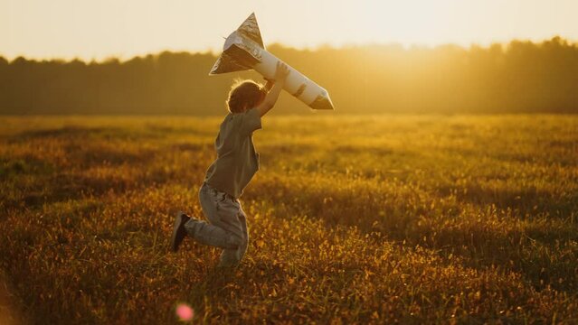 Little Dreamer Boy Holding Handmade Rocket And Running Over Meadow In Summer, Side View, Slow Motion