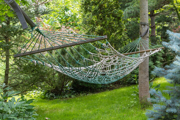 Fragment of braided rope hammock in focus on blurred beautiful green summer garden background. Atmosphere of upcoming vacation. Bright sunny day