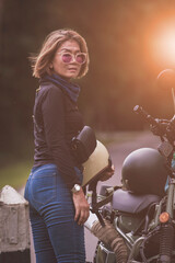 pretty woman holding safety helmet standing on local road beside small enduro motorcycle