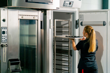 Shot from the back of a girl a pastry chef puts candy to harden in the refrigerator and sets...