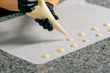 Close-up shot of chocolate being squeezed out of a pastry bag into the shape of natural candies onto parchment in pastry shop  - obrazy, fototapety, plakaty