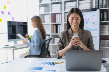 Successful Asian businesswoman smiling using laptop computer and holding coffee cup at office. Confident Asia businesswoman sitting happily in the office.