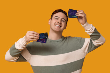 Young man with credit cards on yellow background