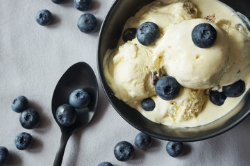 Ice cream with fresh blueberries in a dark plate next to a spoon