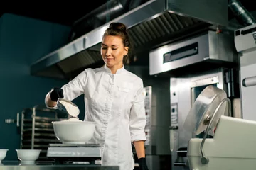 Tuinposter A female baker in  white chef's tunic kneads dough to prepare and bake bread in the bakery © Guys Who Shoot